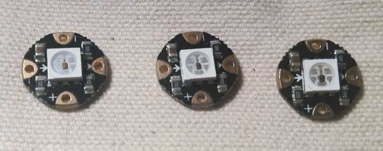 Three wearable NeoPixels laid out such that all arrows face the same direction; the rotation is correct.
