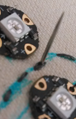 A needle pierces the space between two threads of the power bus, the first stitch of the connection for an individual LED.