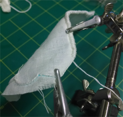 the edge of a piece of linen stretched between two alligator clips, with sewn edging in progress